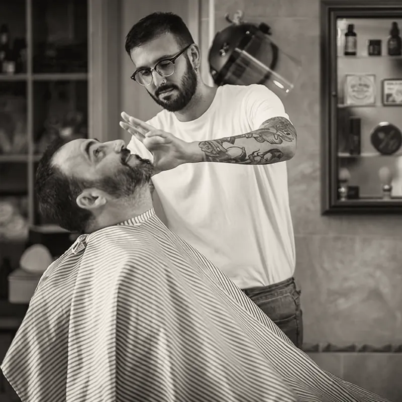 Un barbero arregla la barba de un cliente sentado en el sillón