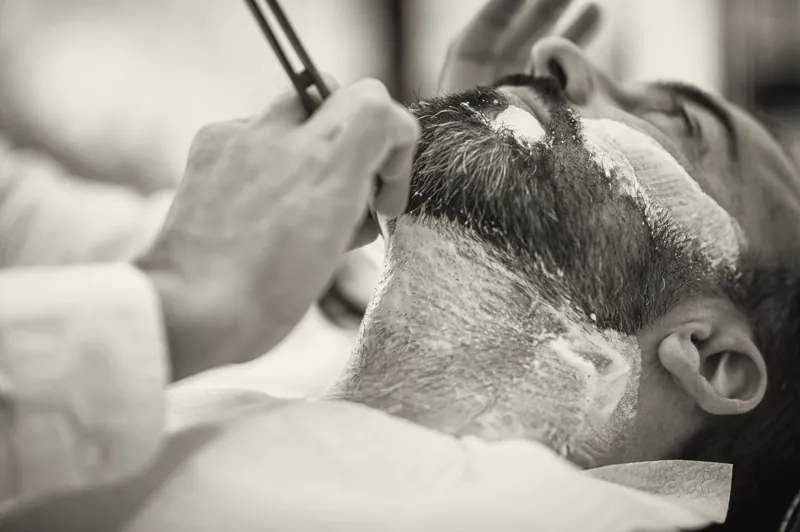 Afeitado a navaja: la hoja recorre la espuma sobre la barba de un cliente