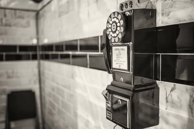 Teléfono antiguo en la pared de azulejos blancos con franja negra